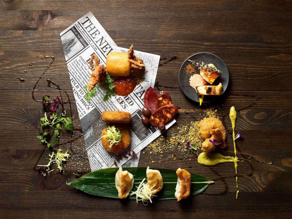 Paradox Singapore Merchant Court At Clarke Quay Εξωτερικό φωτογραφία The photo displays an artistic arrangement of various food items on a dark wooden table. The food is positioned atop a crumpled newspaper, creating a casual yet sophisticated dining presentation. 

There are several pieces of fried food, including wh