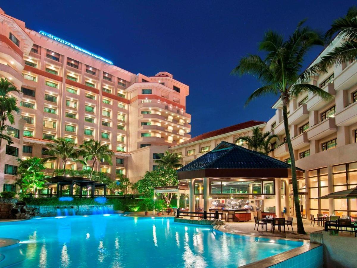 Paradox Singapore Merchant Court At Clarke Quay Εξωτερικό φωτογραφία The photo depicts a luxurious hotel complex set against a twilight sky. In the foreground, there is a large swimming pool that reflects the light from surrounding lights and the sky. Lush greenery, including palm trees, adds to the tropical ambiance.