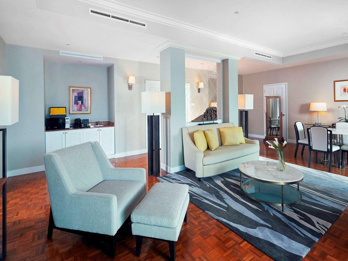 Paradox Singapore Merchant Court At Clarke Quay Εξωτερικό φωτογραφία The photo shows a modern living space, which includes a seating area with a light-colored sofa that has yellow cushions, and an armchair with an ottoman. A round glass coffee table sits in the center on a patterned rug. In the background, there is a 