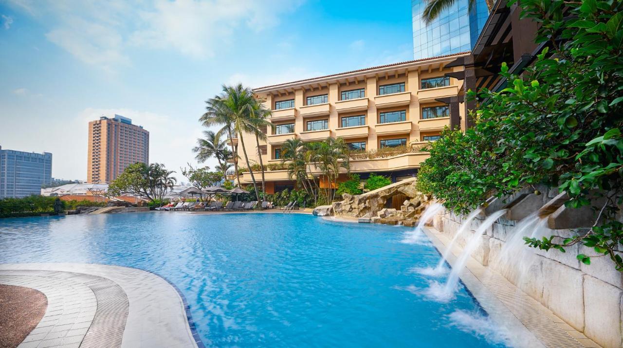 Paradox Singapore Merchant Court At Clarke Quay Εξωτερικό φωτογραφία The photo showcases a scenic hotel resort with a large blue swimming pool in the foreground. The pool features artificial rock formations and small waterfalls cascading gently into the water. Surrounding the pool are lush tropical plants and palm tre