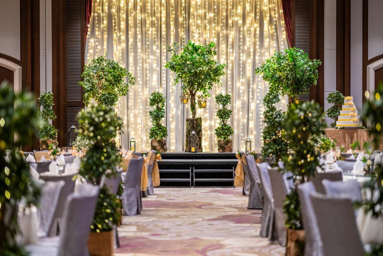 Paradox Singapore Merchant Court At Clarke Quay Εξωτερικό φωτογραφία The image shows an elegantly decorated event space, likely for a wedding or formal celebration. In the center, there is a backdrop with draped fabric illuminated by soft lights, creating a warm ambiance. There are several decorative trees or potted p