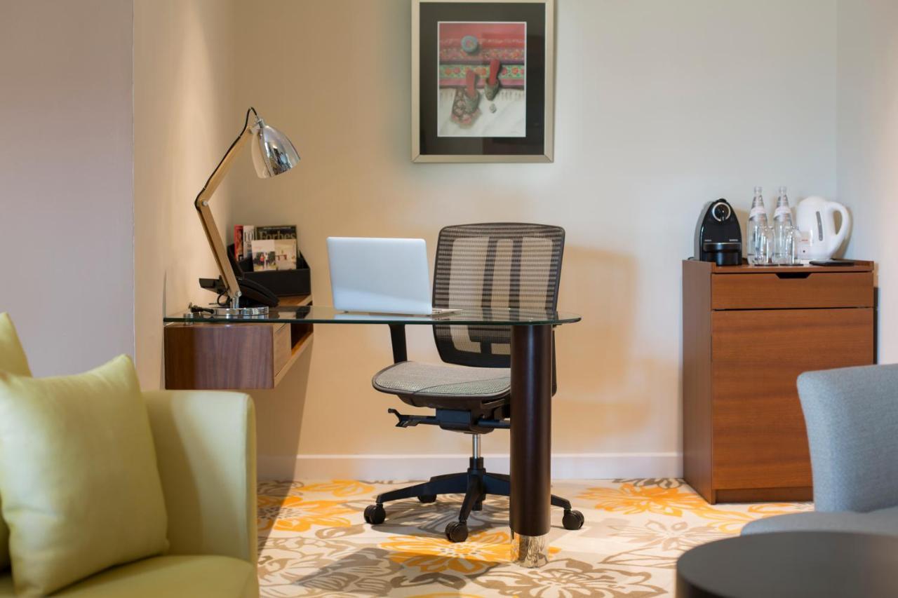 Paradox Singapore Merchant Court At Clarke Quay Εξωτερικό φωτογραφία The photo shows a workspace setup in a well-lit room. It features a modern desk with a glass top and a comfortable office chair. On the desk, there is a laptop and a desk lamp for illumination. To the side, there are some accessories and a coffee mac
