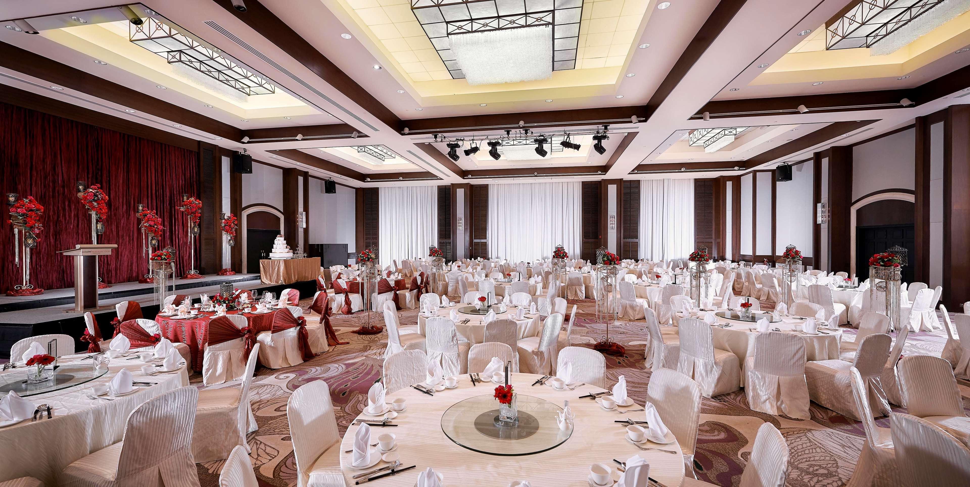 Paradox Singapore Merchant Court At Clarke Quay Εξωτερικό φωτογραφία The photo shows a spacious banquet hall set up for an elegant event. Round tables are beautifully arranged, each covered with a tablecloth and adorned with a center decoration featuring red flowers. The chairs are draped in white covers, adding to th