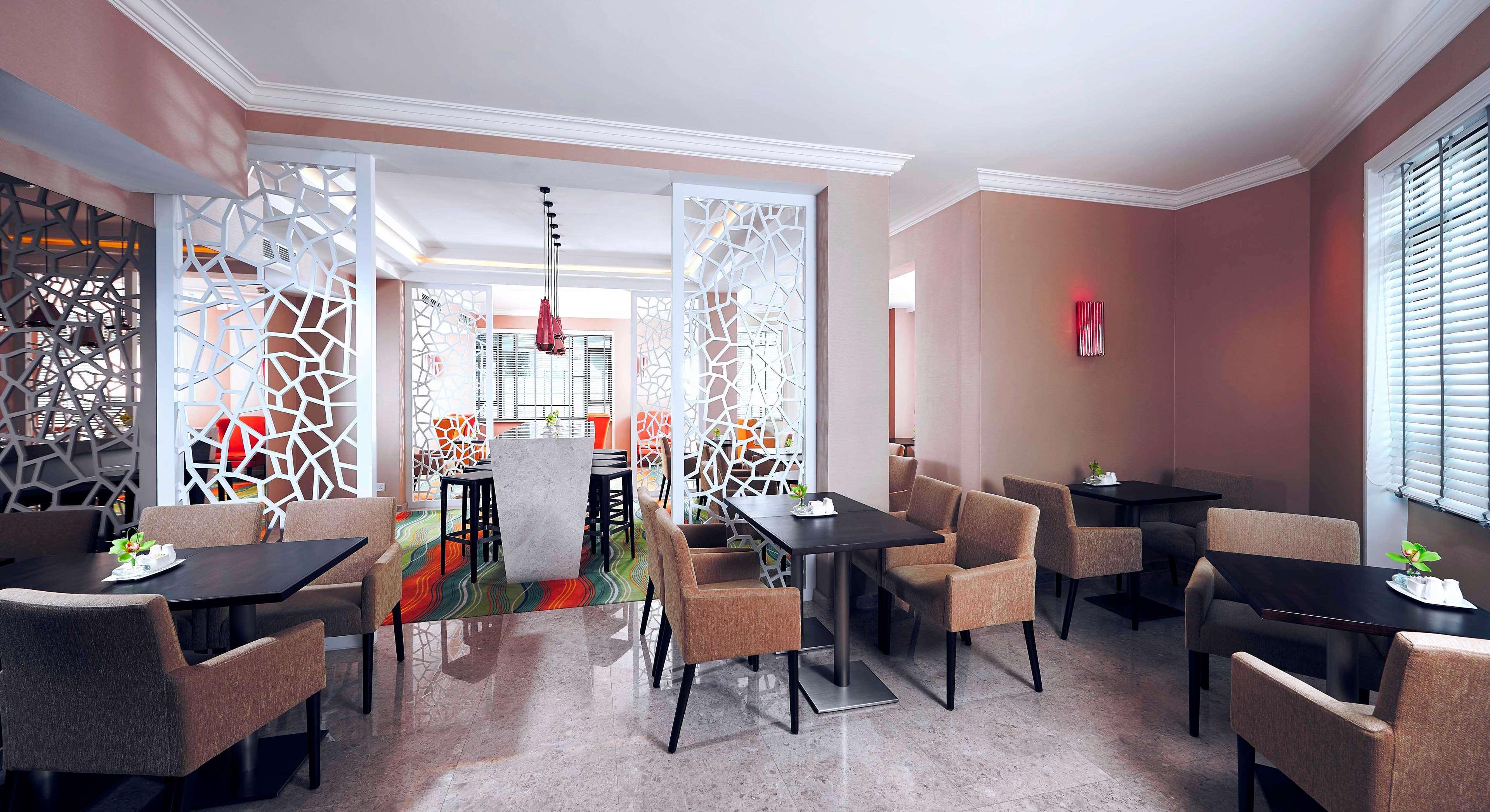 Paradox Singapore Merchant Court At Clarke Quay Εξωτερικό φωτογραφία The image shows an interior view of a modern restaurant or café. It features a well-decorated space with light-colored walls and a polished floor. The dining area has several tables with dark wooden surfaces, surrounded by beige upholstered chairs. 
