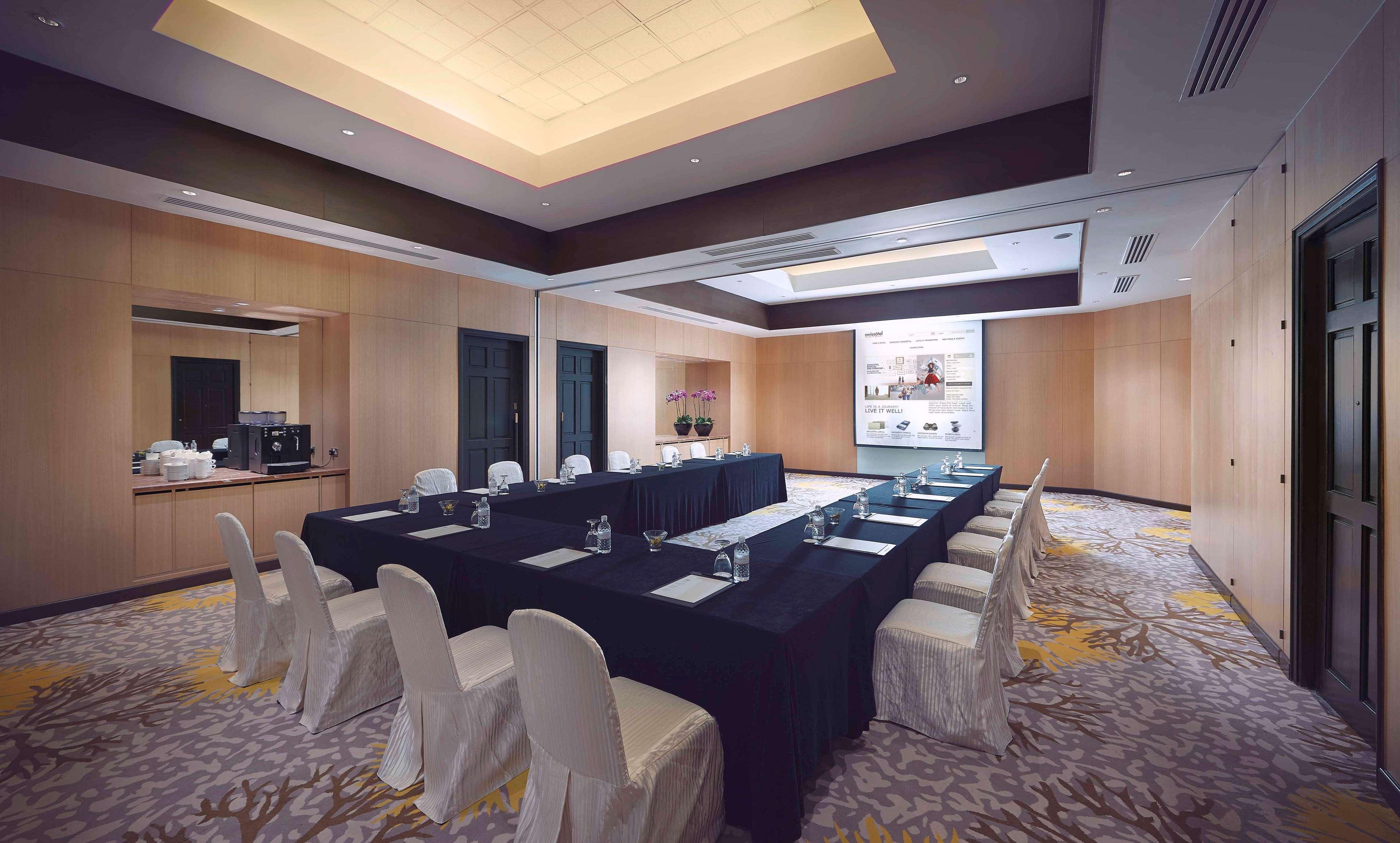 Paradox Singapore Merchant Court At Clarke Quay Εξωτερικό φωτογραφία The photo shows a conference room designed for meetings or presentations. It features a long rectangular table covered with a black tablecloth, surrounded by white chairs. There are glass water pitchers and glasses on the table. The room has wooden p