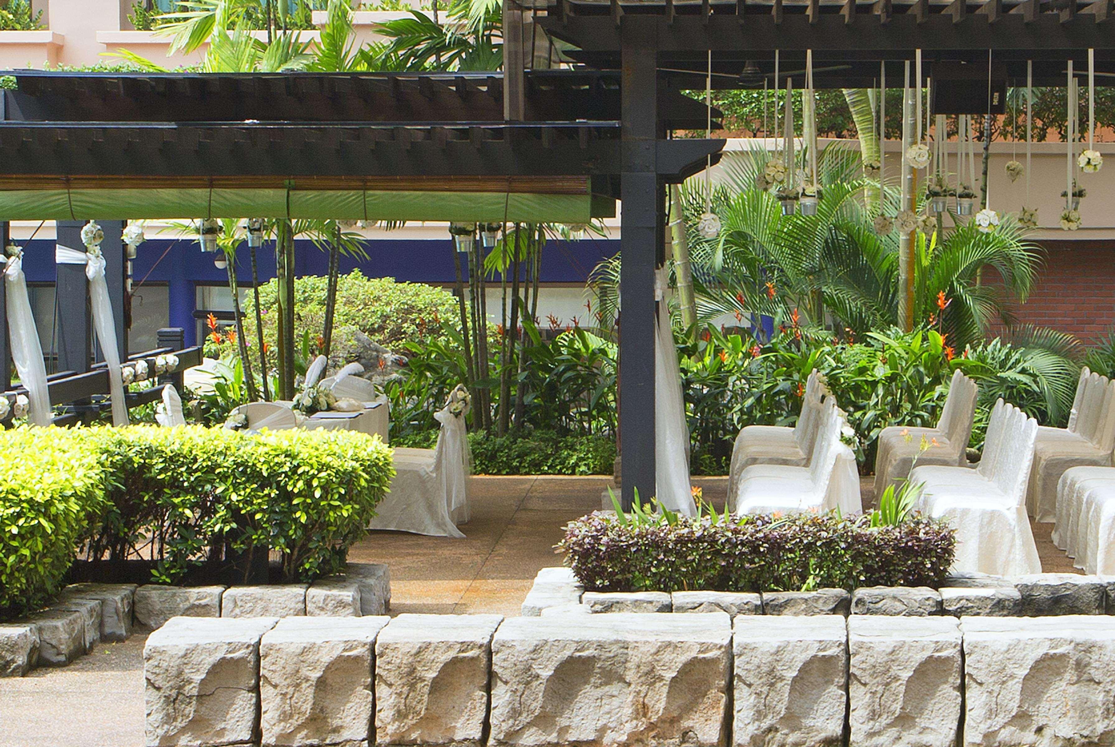 Paradox Singapore Merchant Court At Clarke Quay Εξωτερικό φωτογραφία The image shows a landscaped outdoor area featuring a mix of greenery and seating. There are several white chairs arranged in a relaxed setting under a shaded structure, surrounded by vibrant plants and bushes. In the background, there is a small tab