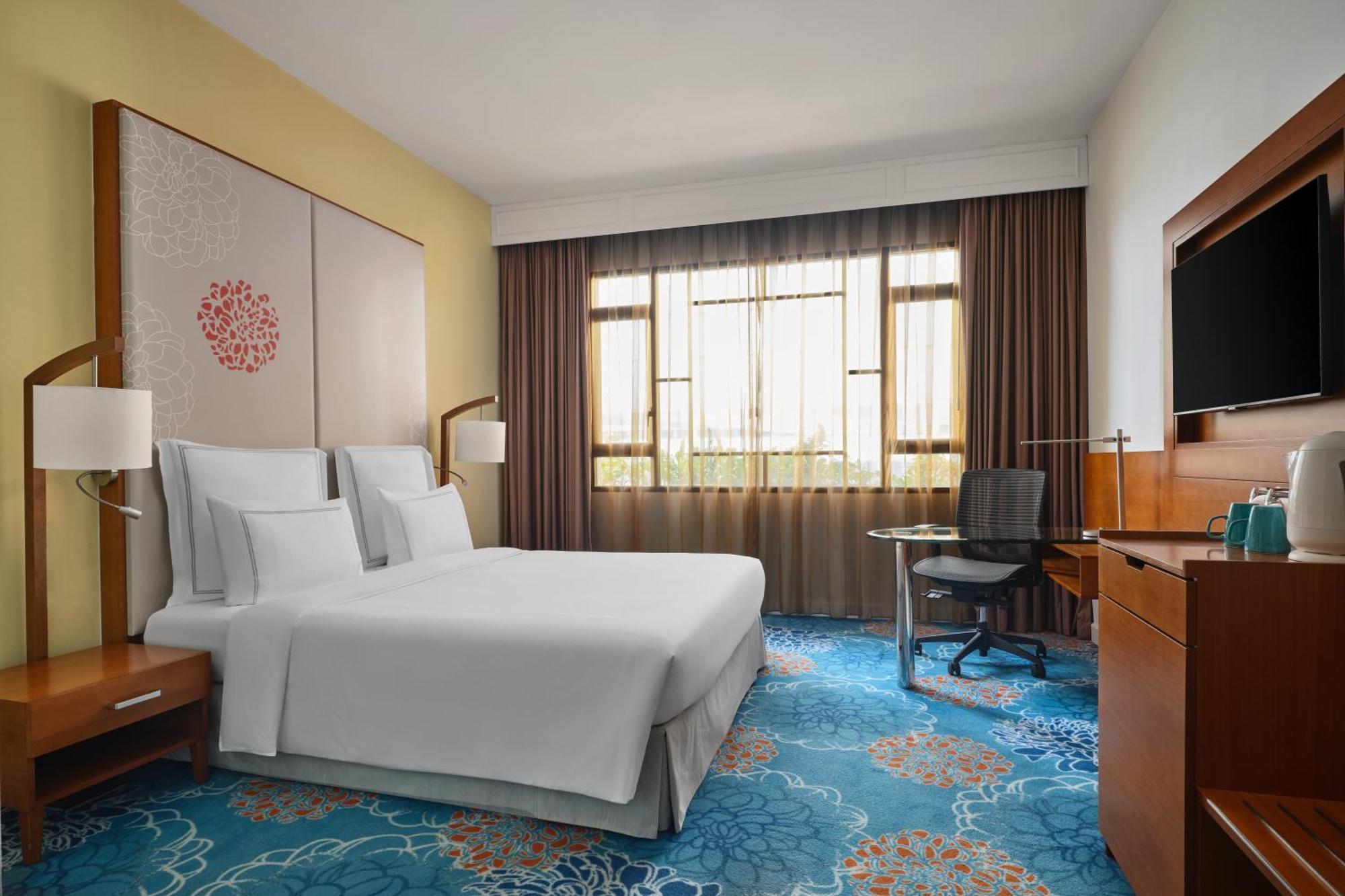 Paradox Singapore Merchant Court At Clarke Quay Εξωτερικό φωτογραφία The photo shows a hotel room featuring a modern and inviting design. It includes a bed with white linens, two bedside lamps, and a decorative wall behind the bed. There is a large window covered with sheer and dark curtains, allowing natural light to